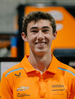 Man with short brown hair smiling with an orange collar shirt